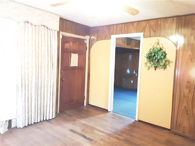 empty room with ceiling fan, wood-type flooring, and wood walls