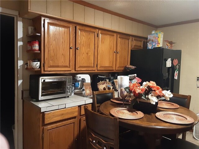 kitchen featuring black refrigerator with ice dispenser, crown molding, and tile counters