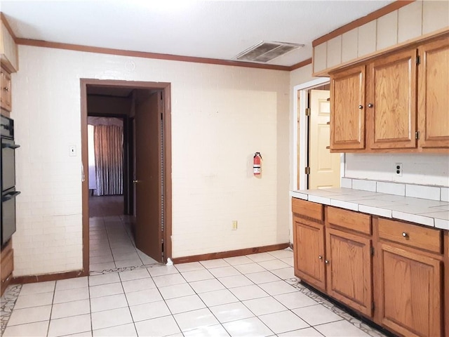 kitchen with brick wall, crown molding, tile countertops, and light tile patterned flooring