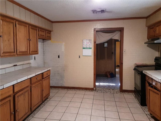 kitchen featuring crown molding, brick wall, black electric range oven, and tile counters