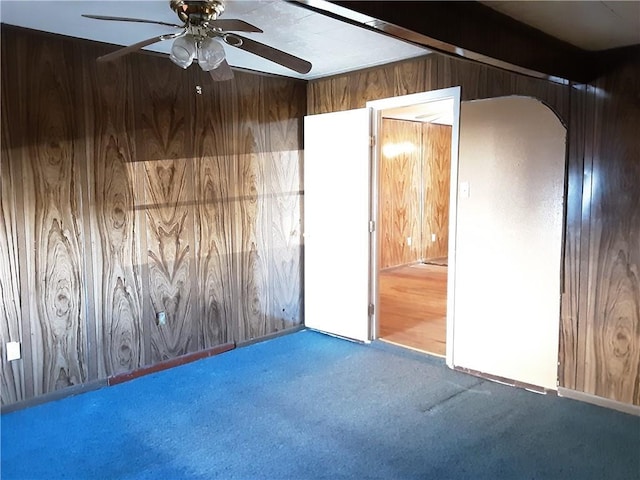 carpeted empty room with ceiling fan and wood walls