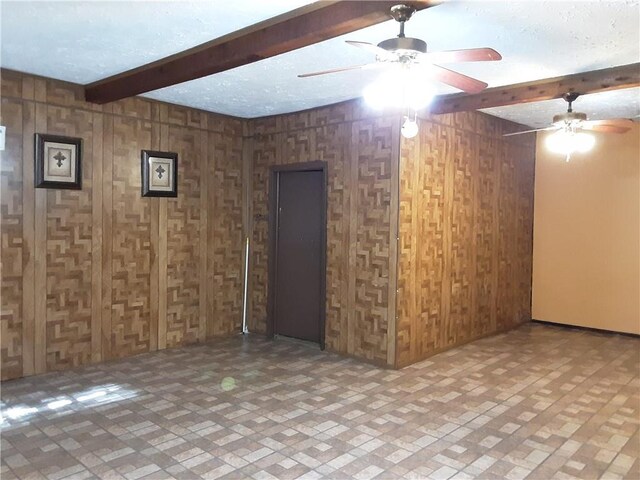 spare room with a textured ceiling, wooden walls, and beamed ceiling