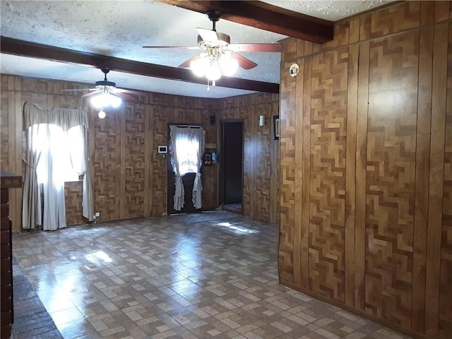 unfurnished room with ceiling fan, a textured ceiling, beamed ceiling, and wooden walls