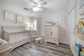 bedroom featuring crown molding, a crib, ceiling fan, hardwood / wood-style floors, and a closet