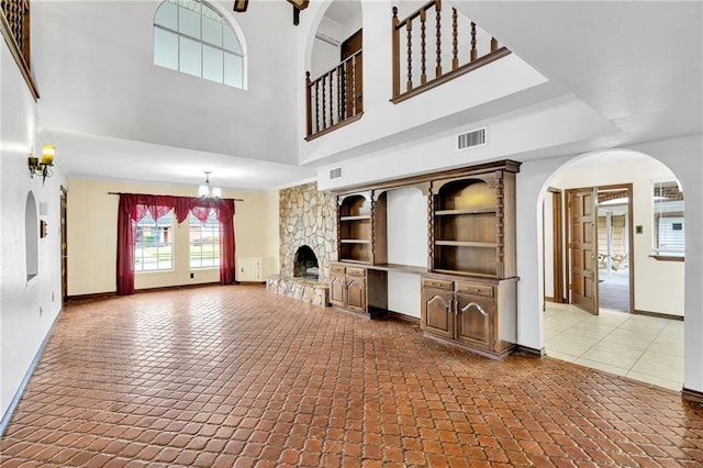 unfurnished living room with built in shelves, a stone fireplace, a notable chandelier, and a high ceiling