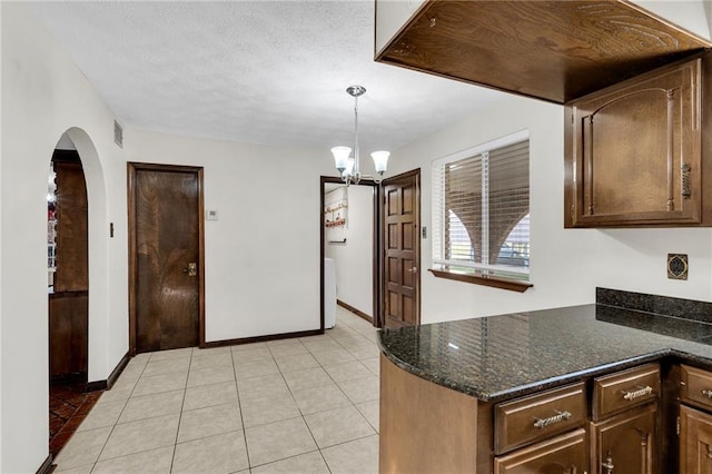 kitchen featuring dark brown cabinets, pendant lighting, a notable chandelier, dark stone countertops, and light tile patterned flooring