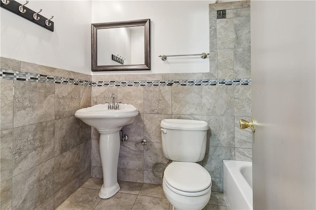 bathroom featuring tile patterned floors, a bathtub, toilet, and tile walls