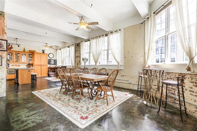 dining room featuring beam ceiling, ceiling fan, and brick wall