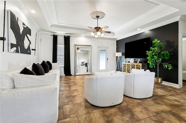 living room featuring a tray ceiling, ceiling fan, and crown molding