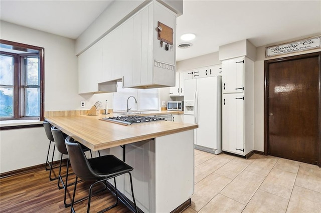 kitchen with appliances with stainless steel finishes, white cabinets, a kitchen breakfast bar, and kitchen peninsula