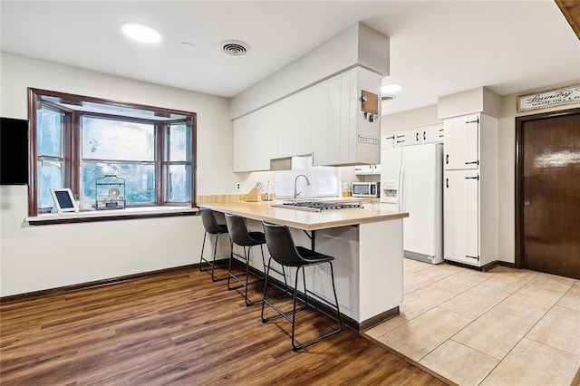 kitchen with kitchen peninsula, white refrigerator with ice dispenser, white cabinets, light hardwood / wood-style floors, and a breakfast bar area