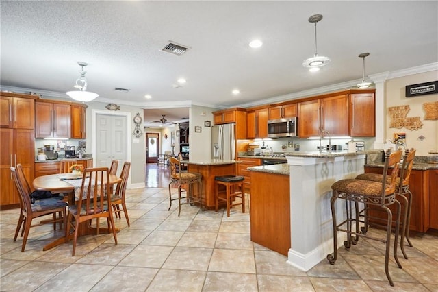 kitchen featuring a kitchen bar, crown molding, stainless steel appliances, and decorative light fixtures