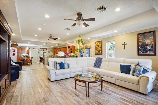 living room with ceiling fan, light hardwood / wood-style floors, a textured ceiling, and a tray ceiling