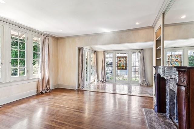 unfurnished living room with built in features, a high end fireplace, wood-type flooring, and ornamental molding