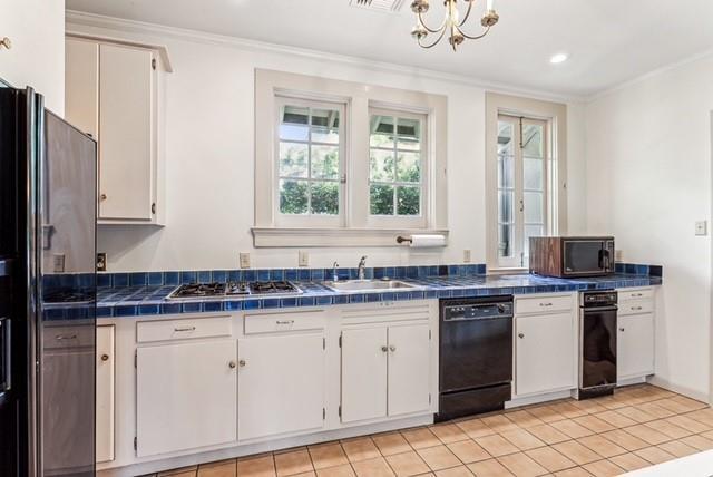 kitchen featuring an inviting chandelier, white cabinets, ornamental molding, tile counters, and stainless steel appliances