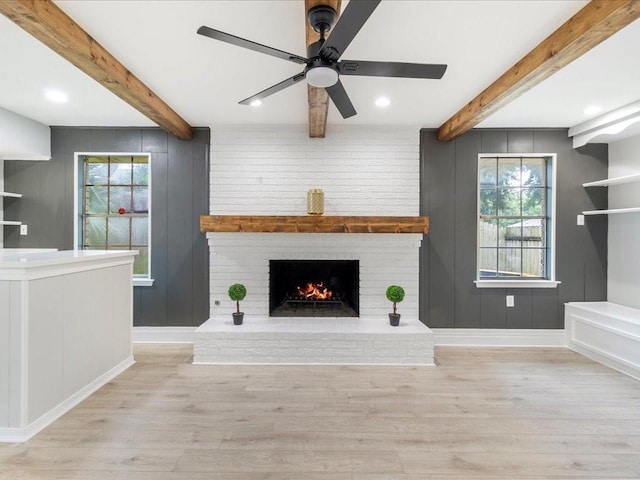 unfurnished living room featuring ceiling fan, beam ceiling, light hardwood / wood-style floors, and a fireplace