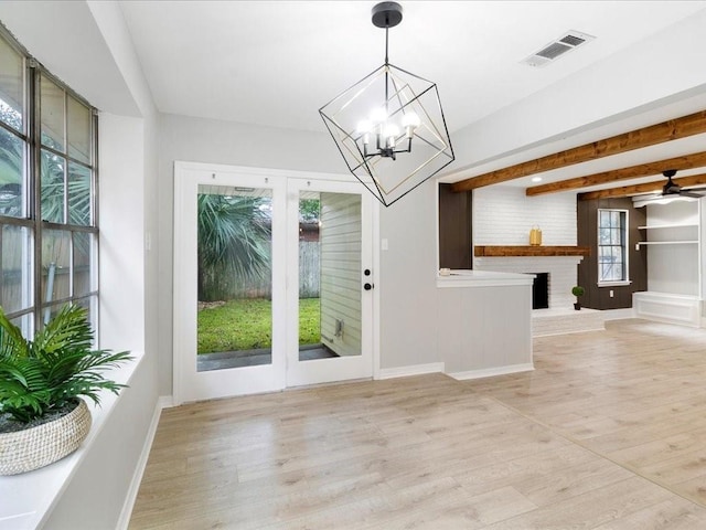 interior space featuring ceiling fan with notable chandelier, light wood-type flooring, a brick fireplace, and beamed ceiling