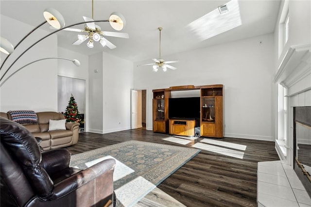 living room with a tile fireplace, ceiling fan, wood-type flooring, and a high ceiling