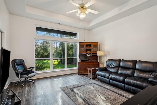 living room featuring a tray ceiling, ceiling fan, and dark wood-type flooring