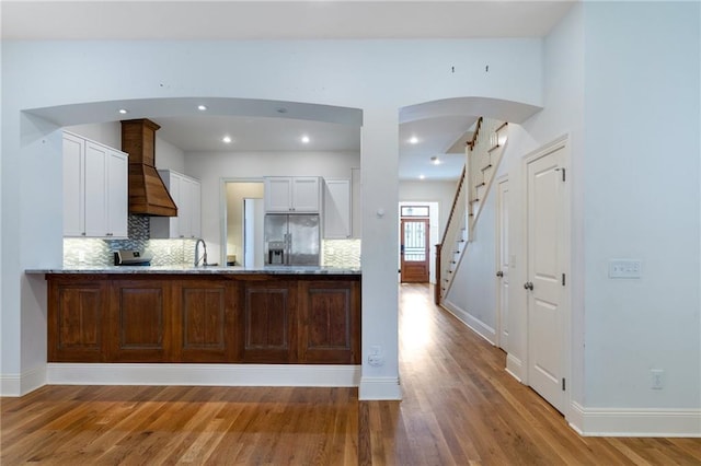 kitchen with custom exhaust hood, light hardwood / wood-style flooring, decorative backsplash, stainless steel fridge, and white cabinetry