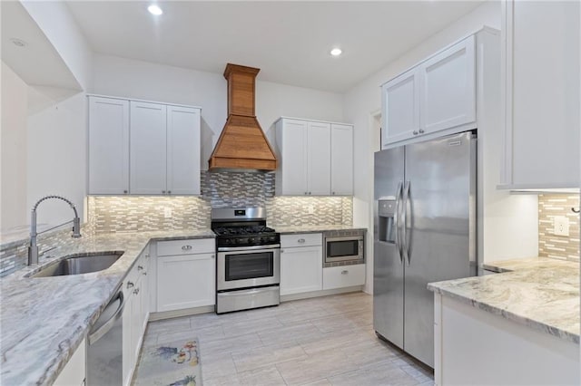 kitchen with premium range hood, white cabinets, sink, appliances with stainless steel finishes, and light stone counters