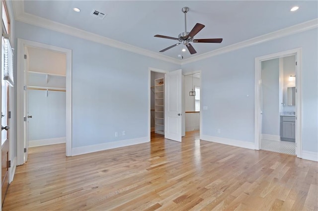 unfurnished bedroom featuring ceiling fan, a spacious closet, crown molding, and ensuite bath