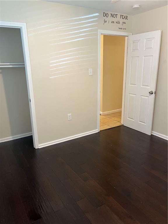 unfurnished bedroom with dark wood-style floors, baseboards, and a closet