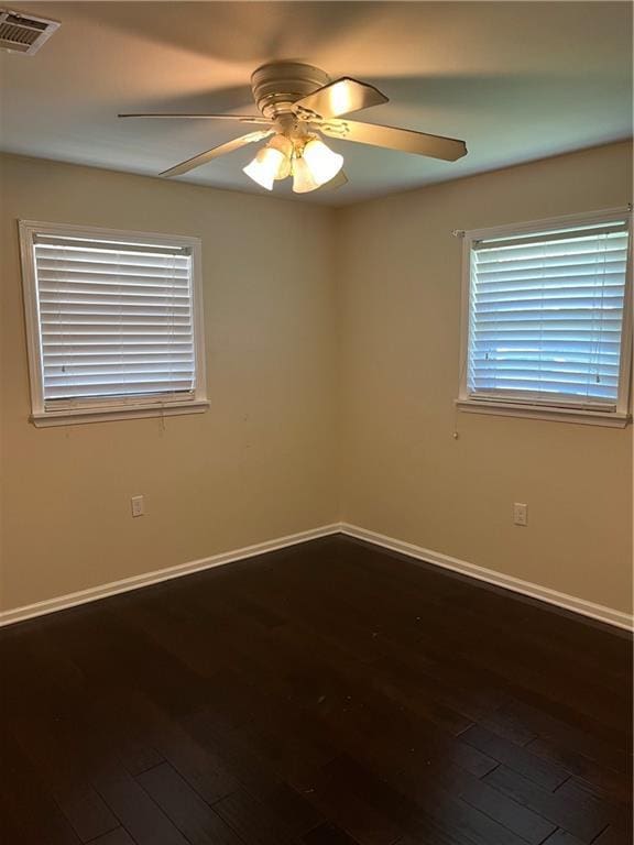 spare room featuring ceiling fan, dark wood-type flooring, visible vents, and baseboards