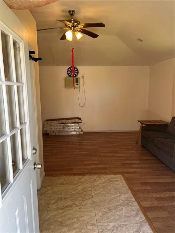 interior space featuring a wall unit AC, a ceiling fan, vaulted ceiling, and wood finished floors