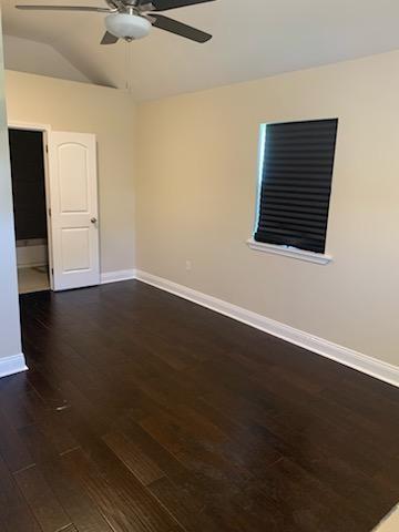 spare room with ceiling fan, vaulted ceiling, baseboards, and dark wood finished floors