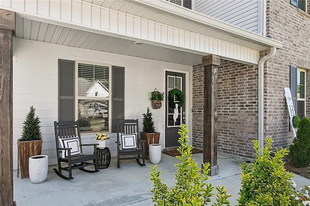 view of exterior entry with a porch and brick siding