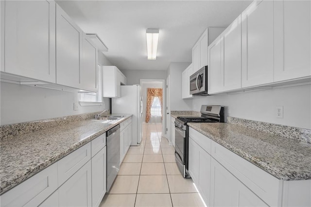 kitchen featuring white cabinets, light tile patterned floors, stainless steel appliances, and light stone counters