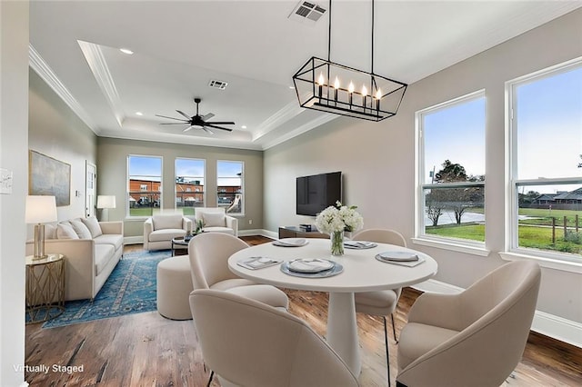 dining space with ornamental molding, wood-type flooring, a tray ceiling, and ceiling fan with notable chandelier