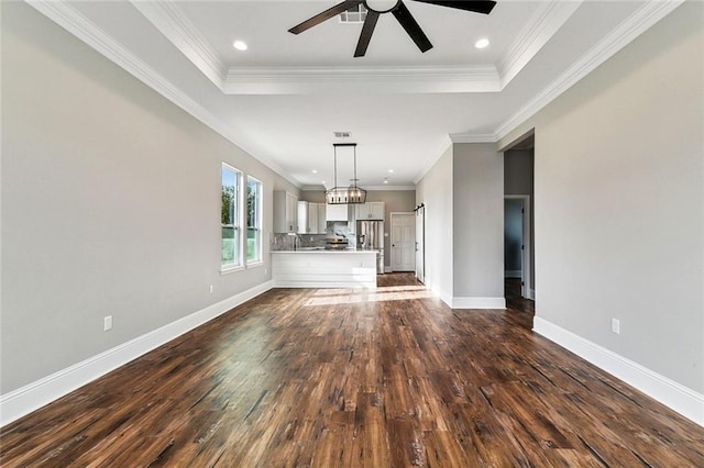 unfurnished living room with dark hardwood / wood-style flooring, a tray ceiling, ceiling fan with notable chandelier, and ornamental molding