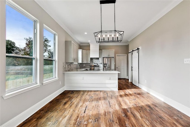 kitchen featuring crown molding, stainless steel fridge, kitchen peninsula, decorative backsplash, and a barn door