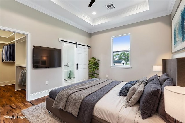 bedroom with dark wood-type flooring, a tray ceiling, ornamental molding, a spacious closet, and a barn door