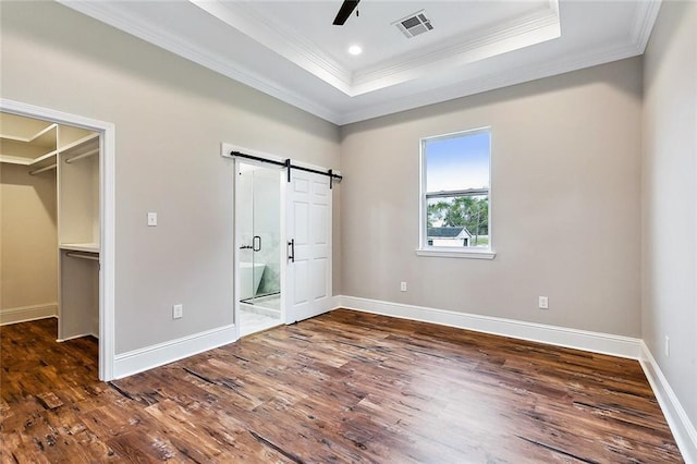 unfurnished bedroom featuring dark wood-type flooring, a tray ceiling, a barn door, and a spacious closet