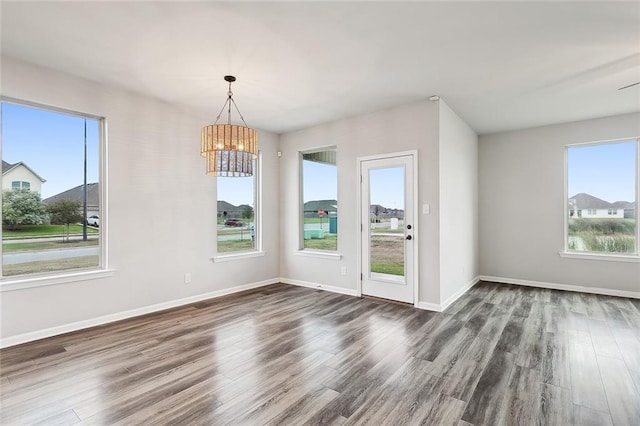 unfurnished dining area featuring dark wood-type flooring, a wealth of natural light, and a notable chandelier