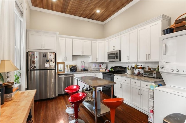 kitchen with white cabinets, stainless steel appliances, stacked washer / dryer, and wood ceiling