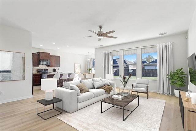 living room with ceiling fan with notable chandelier and light wood-type flooring