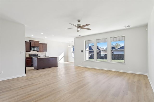 unfurnished living room featuring ceiling fan with notable chandelier, light wood-type flooring, and sink