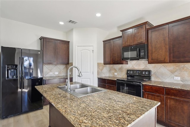 kitchen with sink, tasteful backsplash, an island with sink, light hardwood / wood-style floors, and black appliances