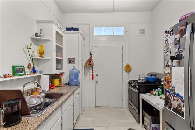 kitchen featuring light countertops, open shelves, white cabinets, appliances with stainless steel finishes, and a sink