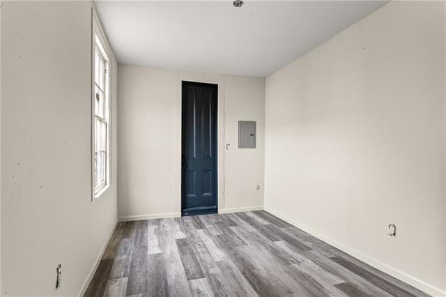 unfurnished room featuring a healthy amount of sunlight, electric panel, baseboards, and wood finished floors