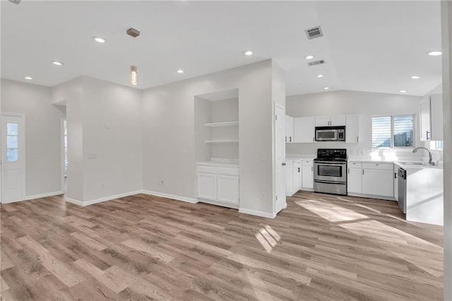 interior space featuring appliances with stainless steel finishes, light wood-type flooring, built in shelves, white cabinets, and hanging light fixtures