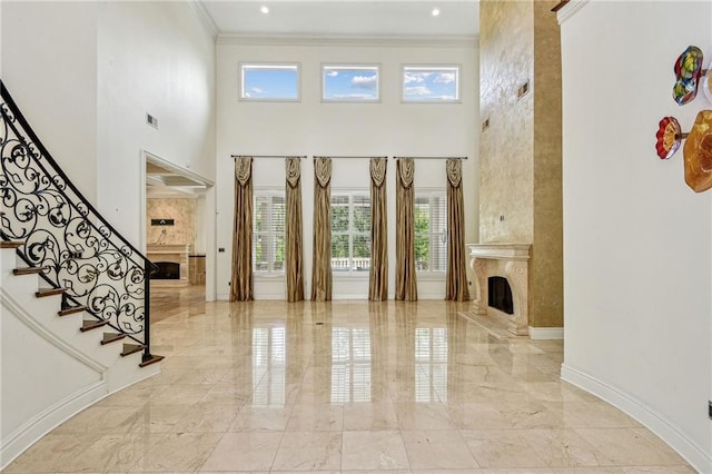 entrance foyer with a premium fireplace, a towering ceiling, and crown molding