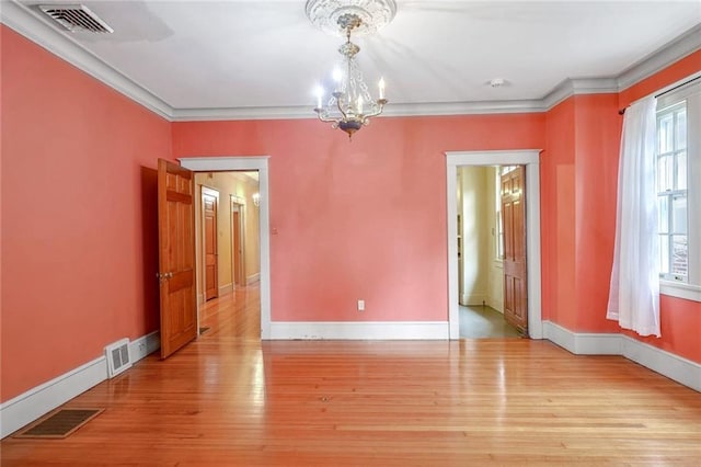 spare room featuring light wood-type flooring, ornamental molding, and a chandelier