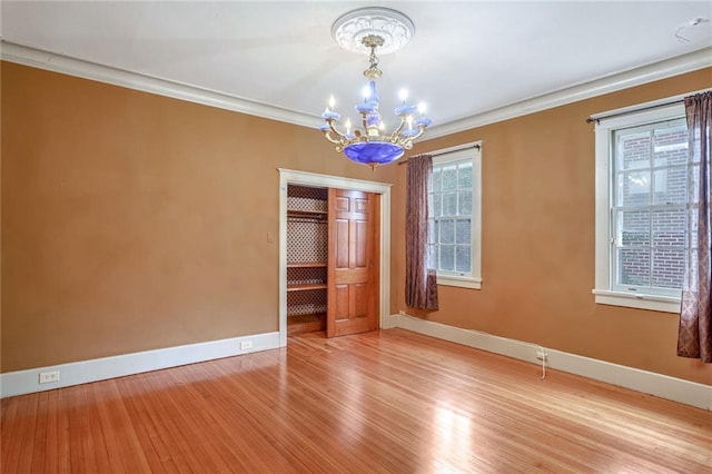 spare room featuring wood-type flooring, crown molding, and a notable chandelier