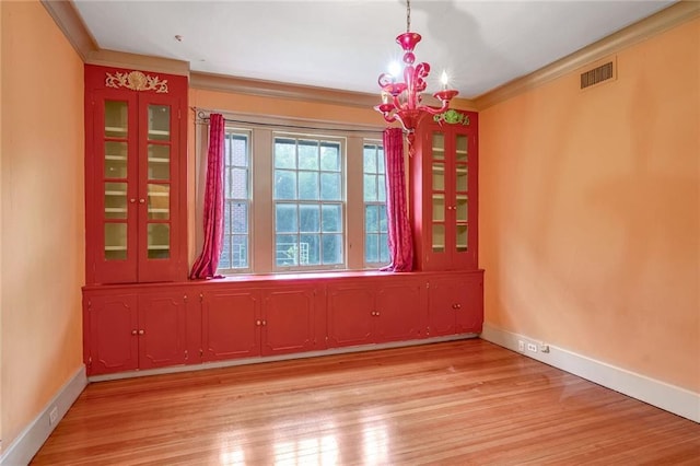 unfurnished dining area with a chandelier, light hardwood / wood-style floors, and ornamental molding