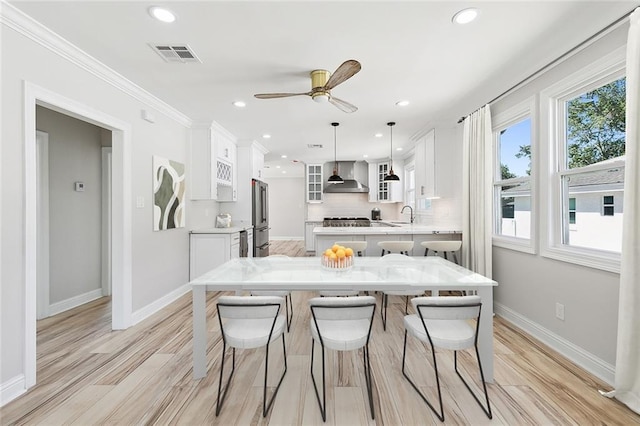 kitchen featuring wall chimney exhaust hood, a breakfast bar, white cabinetry, decorative light fixtures, and high quality fridge